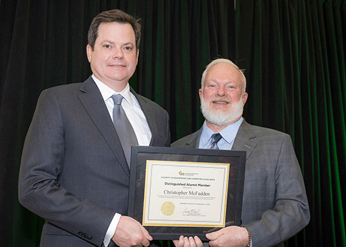 Two men in gray suits and white shirts hold award certificate